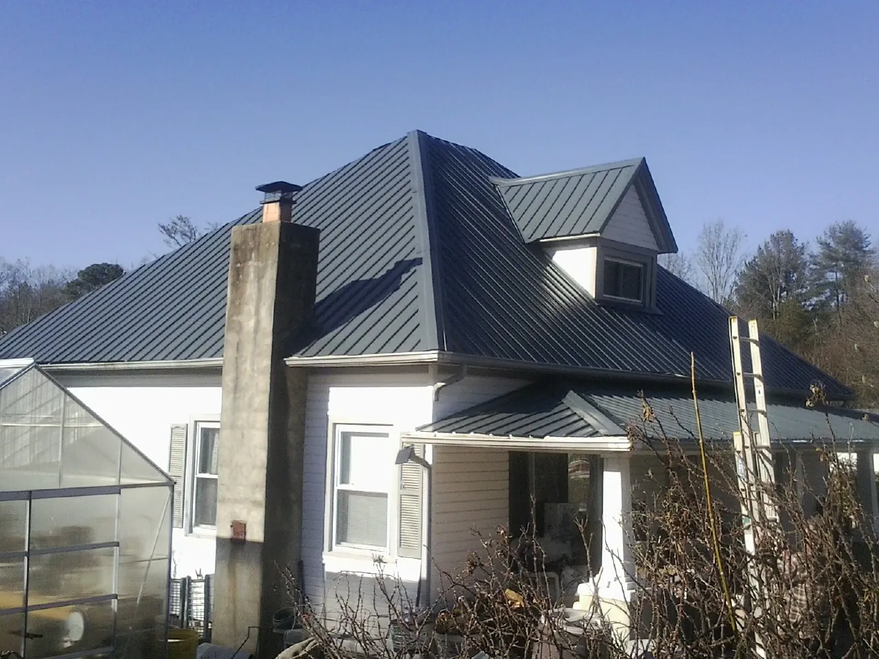 Dark blue standing seam metal roof on a white farmhouse with dormer — Slate & Tile Roof Repair by Roofing Brothers in Marlow