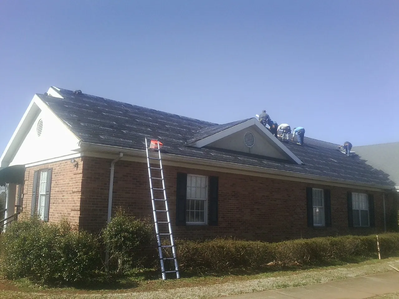 Crew tearing shingles off a brick ranch roof with a ladder set — Metal Roof Repair work by our crew in Marlow
