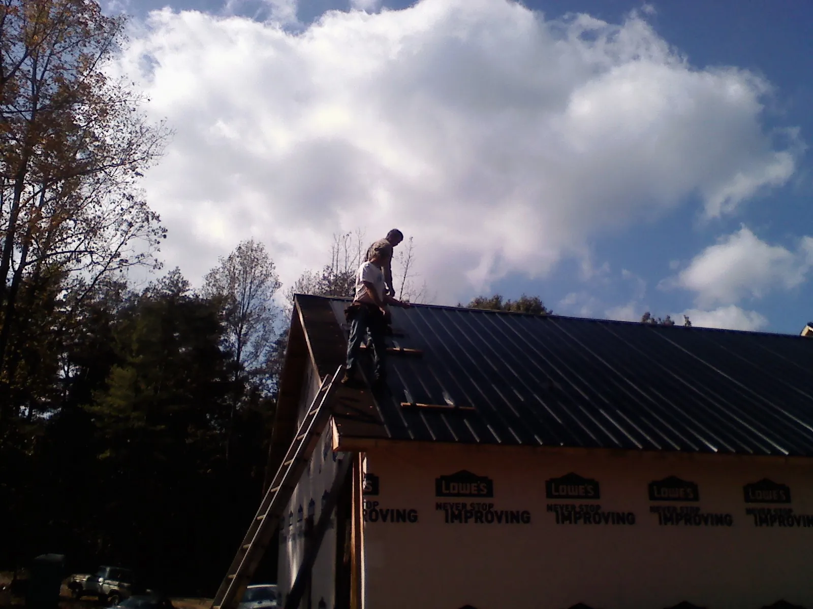 Roofer fastening dark metal panels high against a cloudy sky, from a Roof Inspection job in Marlow